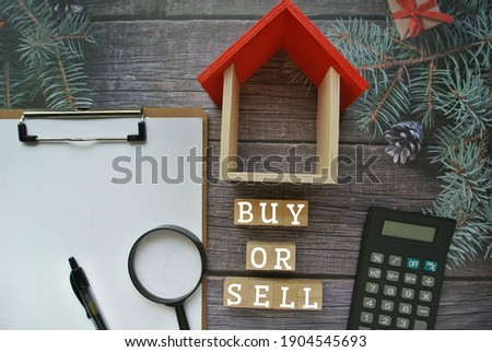 Word BUY or SELL on wooden block inscription with calculator, fake house, pen and paper on table. House loan, business, financial concept.