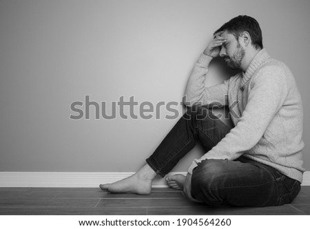 Portrait of a caucasian man in his 40s who is wearing jeans and a sweater. He looks depressed with his hands on his head. The photo is black and white.  Royalty-Free Stock Photo #1904564260