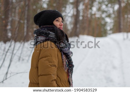 A young girl in a black hat and brown jacket stands in the winter forest and looks into the distance. High quality photo