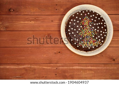 CAKE. chocolate cake decorated with a Christmas tree and white snowflakes. on a white plate. on a wooden background. Christmas and New Years concept. view from above. place for text