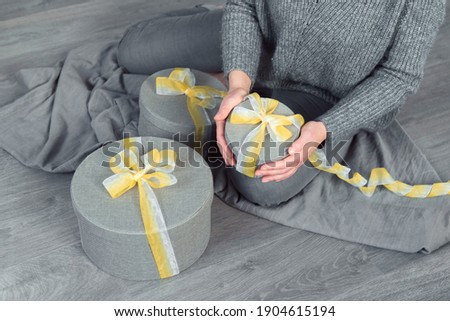 woman hands pack gifts, grey round box yellow ribbon