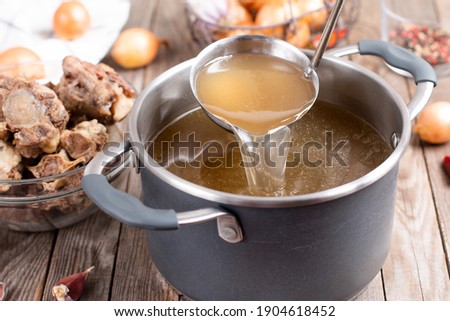 Saucepan with bouillon with a ladle on the table. Bone broth Royalty-Free Stock Photo #1904618452