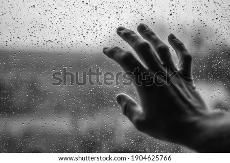 Hand on a rain-soaked window pane with a view outside Royalty-Free Stock Photo #1904625766