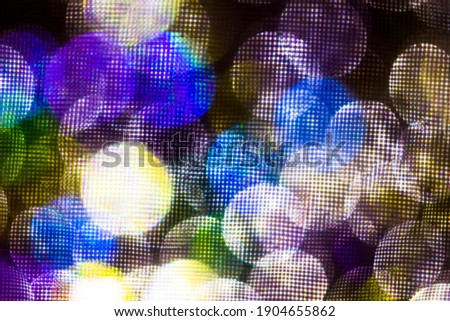 Out of focus color lights through the sieve. Blurred bokeh lights with led panel effect. Abstract background with glowing, glitter particles