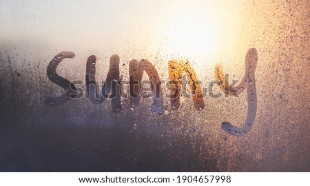 The sunny word on the steamy window with water drops on sunny background. fogged window at home