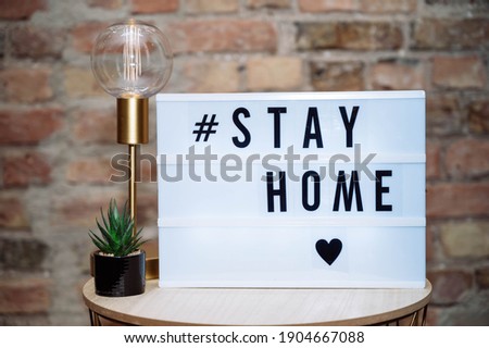 COVID-19 Coronavirus staying at home lightbox message sign. Text hashtag #STAY HOME glowing in light to promote self isolation staying at home isolated on brick wall background.