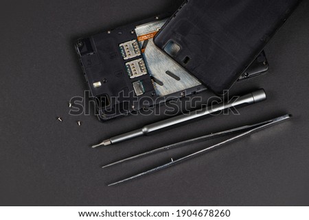 Broken mobile phone and repair tools on dark background, flat lay
