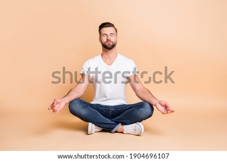 Portrait of nice calm focused guy sitting on floor meditating relaxation isolated over beige pastel color background