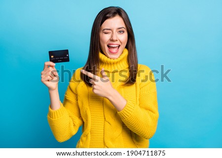 Photo of impressed flirty young woman dressed yellow pullover winking pointing bank card isolated blue color background