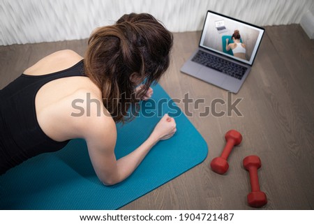Young sporty slim woman has internet video online fitness training instructor modern laptop screen. Healthy lifestyle concept, online fitness and sport lessons. Plank exercise Royalty-Free Stock Photo #1904721487