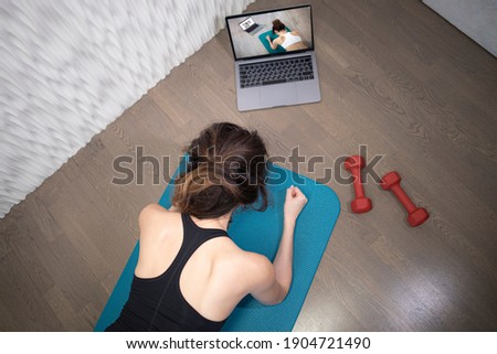 Young sporty slim woman has internet video online fitness training instructor modern laptop screen. Healthy lifestyle concept, online fitness and sport lessons. Plank exercise Royalty-Free Stock Photo #1904721490