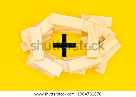 a plus sign and the wooden blocks on a yellow background.
