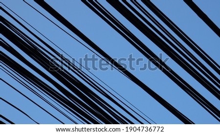Many electricity wires ran streaked through the bright blue sky at day time. Silhouette photo. Upward angle.