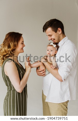 Young parents hug and kiss their newborn daughter on a white background in the studio.
