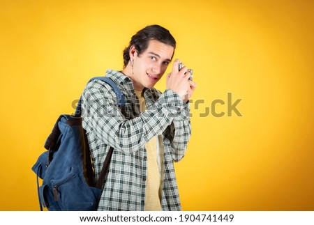 Happy smiling handsome young man, caucasian, with a camera and backpack, digital nomad, traveler, yellow background, copy space.