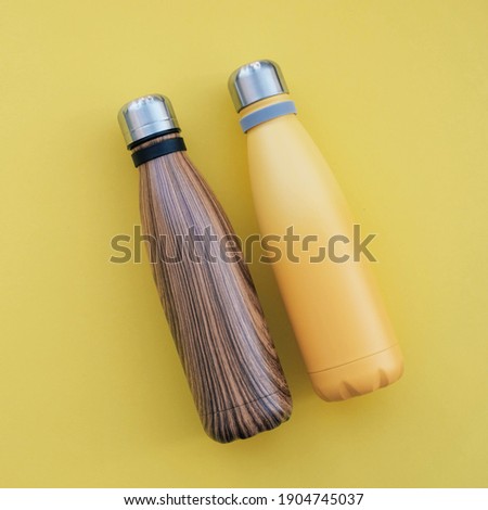 Reusable eco friendly metal water bottles on yellow background, top view. Copy space for text. Zero waste and sustainable lifestyle.