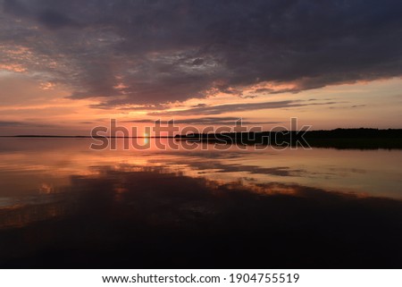 Sky in the brightly lit twilight of a sunset over picturesque  lake water with  reflection clouds and  sunbeam on the horizon over the water surface