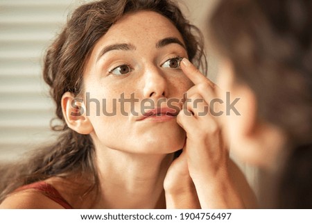 Young woman trying to apply contact lenses in front of a mirror. Young woman trying on new contact lenses. Close up of a girl trying on beauty medical contact-lenses. Royalty-Free Stock Photo #1904756497