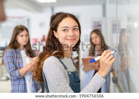 Portrait of smiling girl solving math equation on white board. College student thinking and solving arithmetic sum with classmates. Smart young woman writing on white board during class. Royalty-Free Stock Photo #1904756506