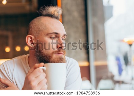 Brutal man of European appearance in a cafe in the morning with a cup of hot coffee