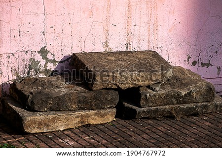 Picture of old dusty square shape stone kept in front of wall.