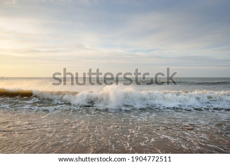 Baltic sea shore (sand dunes) at sunset. Soft sunlight, clear sky with glowing clouds, waves and water splashes. Idyllic seascape. Liepaja, Latvia, Europe. Warm winter weather, climate change, nature Royalty-Free Stock Photo #1904772511