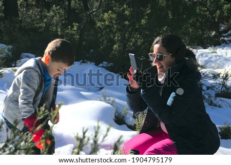 Mother takes a picture with a smartphone of her child in the snow