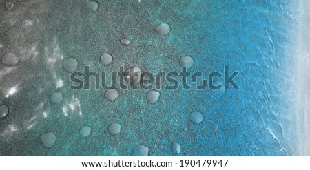 volcanic sea shore, with placed sea shells between stones and fine sand, all in black, with water reflections, fading into blue