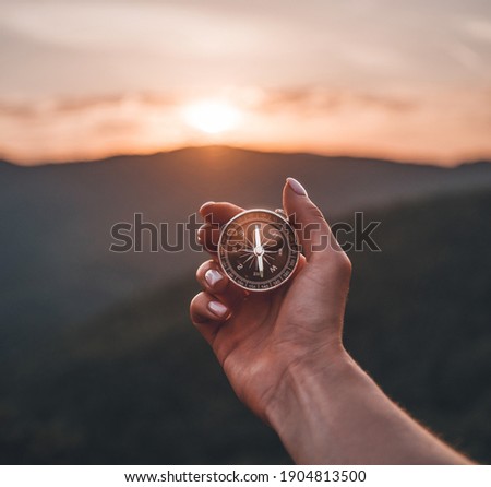 Traveler explorer young woman holding compass in a hand in summer mountains at sunrise, point of view. Royalty-Free Stock Photo #1904813500