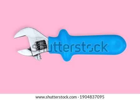 Adjustable metal wrench with a rubberized handle on a pink background.