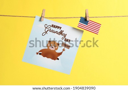 Happy Groundhog Day greeting card and American flag hanging on yellow background