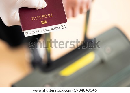 (Selective focus) Overhead view of an human hand wearing a latex glove, holding a passport with 'Covid-19 Vaccinated' label inside it. Travel concept during the Covid-19 pandemic. Royalty-Free Stock Photo #1904849545
