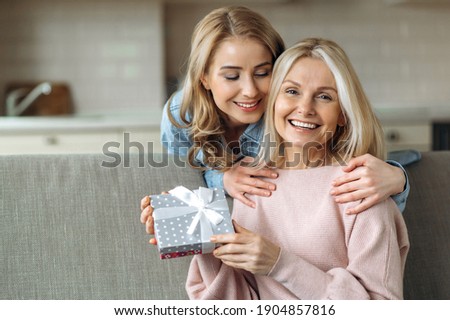Loving young adult daughter makes an unexpected surprise to her mature attractive mom, gives her a gift. Friendship of mom and daughter