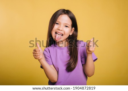 The cheerful girl makes faces and shows her tongue. Leisure of the child. Studio photo on a yellow background