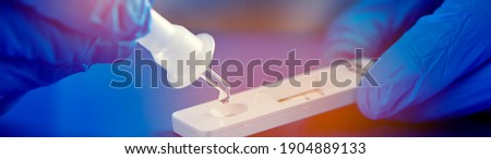 a healthcare worker, wearing blue surgical gloves, places the sample into the covid-19 antigen diagnostic test device, in a panoramic format to use as header or web banner Royalty-Free Stock Photo #1904889133