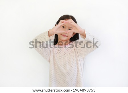 Asian little child girl making fingers for heart sign on eyes on white background. Focus at his finger