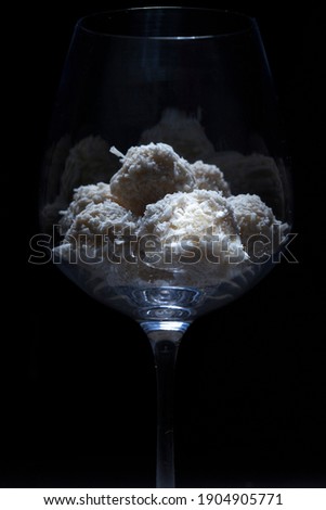 
Homemade candies of white chocolate and coconut in a glass on a black background. Rafaello