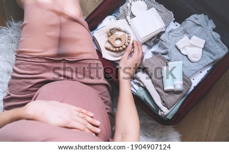 Pregnant woman hugging belly and packing maternity hospital bag. Beautiful mother during pregnancy waiting for baby preparing suitcase of clothes, toy and necessities for newborn child birth. Royalty-Free Stock Photo #1904907124