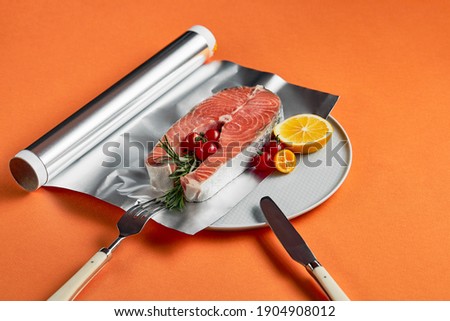 fresh salmon with lemon in foil paper, ready for cooking in oven on orange background Royalty-Free Stock Photo #1904908012