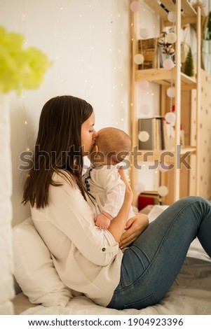 mom sits with her daughter on the bed and kisses her. Mom and daughter don't look at the camera