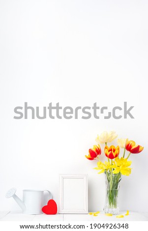 Tulip flower in glass vase with picture frame on white wall, Mother's Day decor concept.
