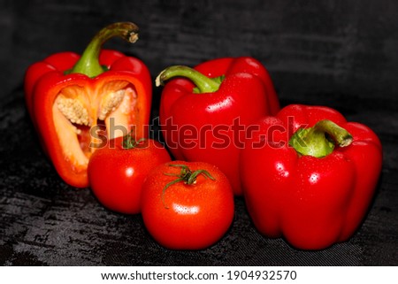 Red pepper and tomatoes are lying on the black background. Close-up, top view. Print for kitchen