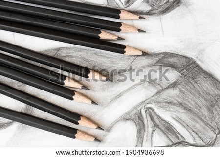 set of wooden graphite pencils on hand-drawn academic drawing of male face close up