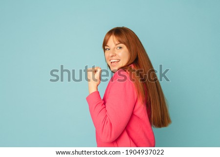 Powerful. Caucasian woman's portrait isolated on blue studio background with copyspace. Beautiful female model in pink sweatshirt. Concept of human emotions, facial expression, sales, ad, fashion.