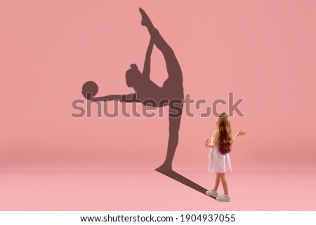 Childhood and dream about big and famous future. Conceptual image with girl and drawned shadow of female rhythm gymnast on coral pink background. Childhood, dreams, imagination, education concept.