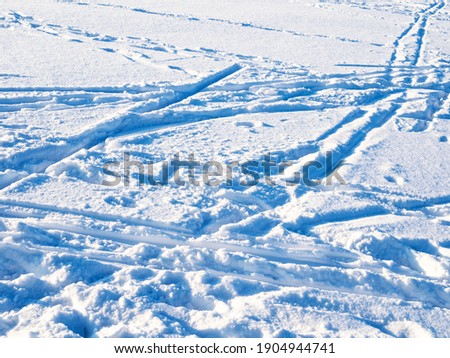blue surface of snow with ski tracks and footprints lit by setting sun in cold winter twilight