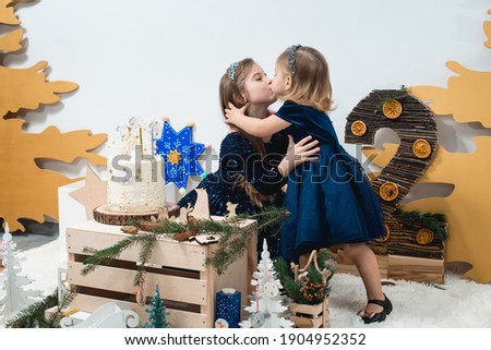 Children's winter birthday decorations. Cute little girls in a blue dresses hugging near white birthday cake