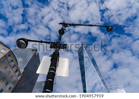 View looking up at the sky with a tall lamp post in the center of frame, surrounded by buildings and the Freedom Tower