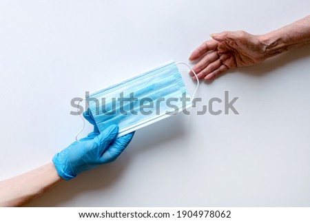 The doctor's hands in medical gloves on a white background pass the mask to an elderly woman