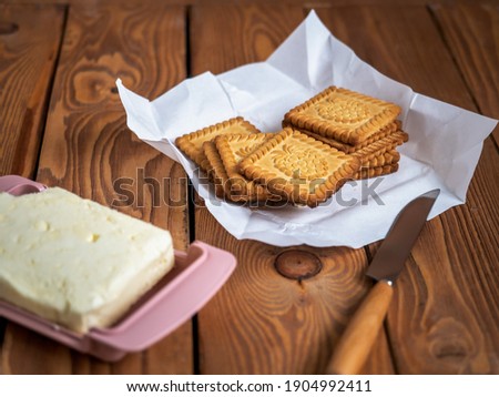 Cookies with a picture of raspberries on brown paper and butter in a butter dish and a kitchen knife on a wooden tray